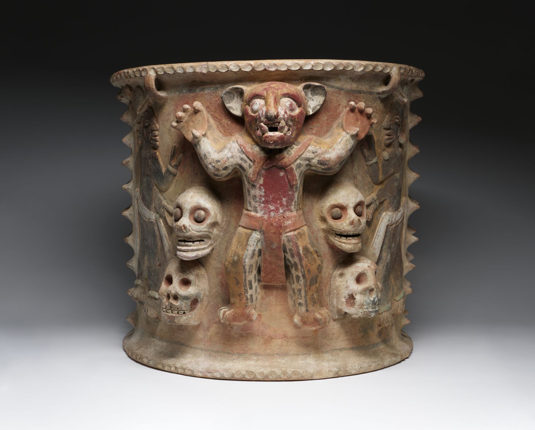 a ceramic urn depicting a person wearing a jaguar costume surrounded by four human skulls