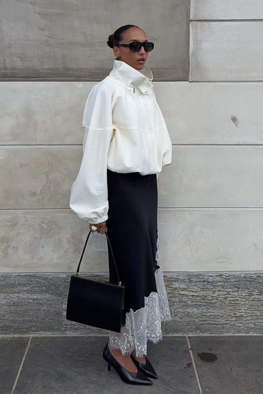a woman wearing a white jacket, black lace-trim skirt, and black pointed toe heels