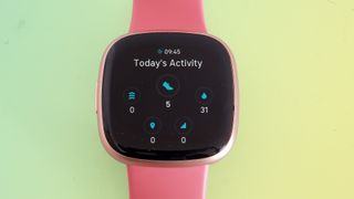 En närbild på urtavlan på en Fitbit Versa 4 med ett rosa armband.