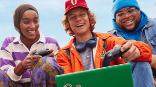 Three college students holding gaming controllers and playing a game on a laptop