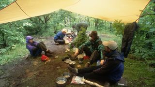 How to camp in the rain: a group of campers hang out under a tarp