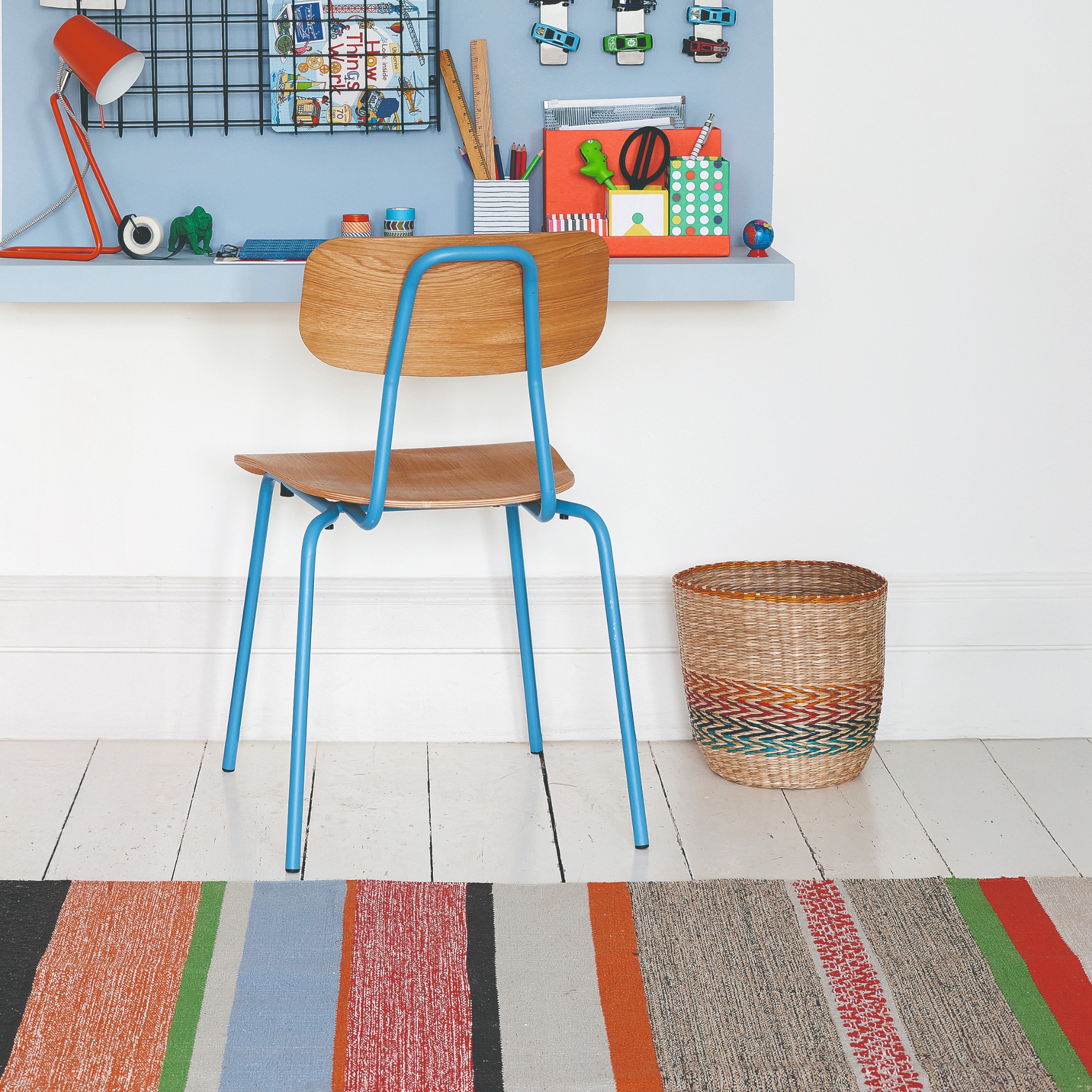 A desk area painted light blue with a striped rug on a white wooden floor