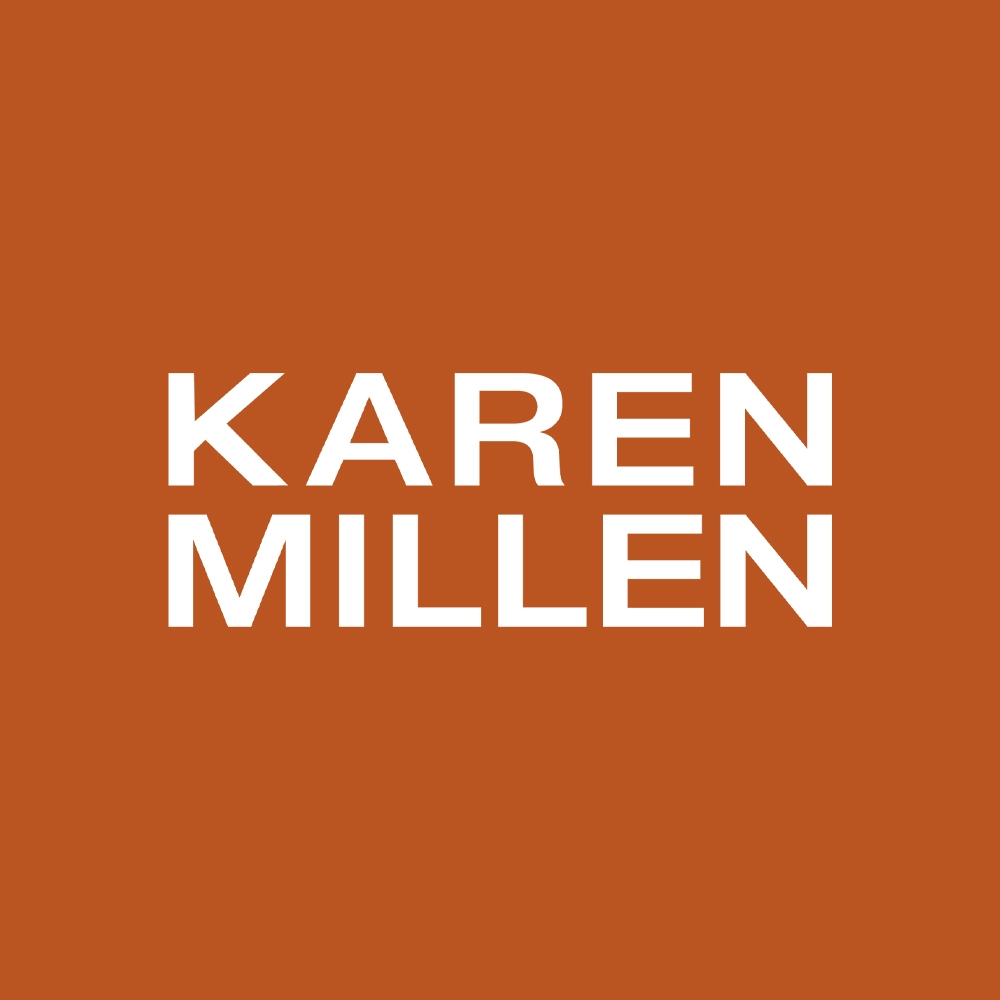 Woman staring at camera, sat on garden bench wearing a Karen Millen white dress with green bow and leaves on it.