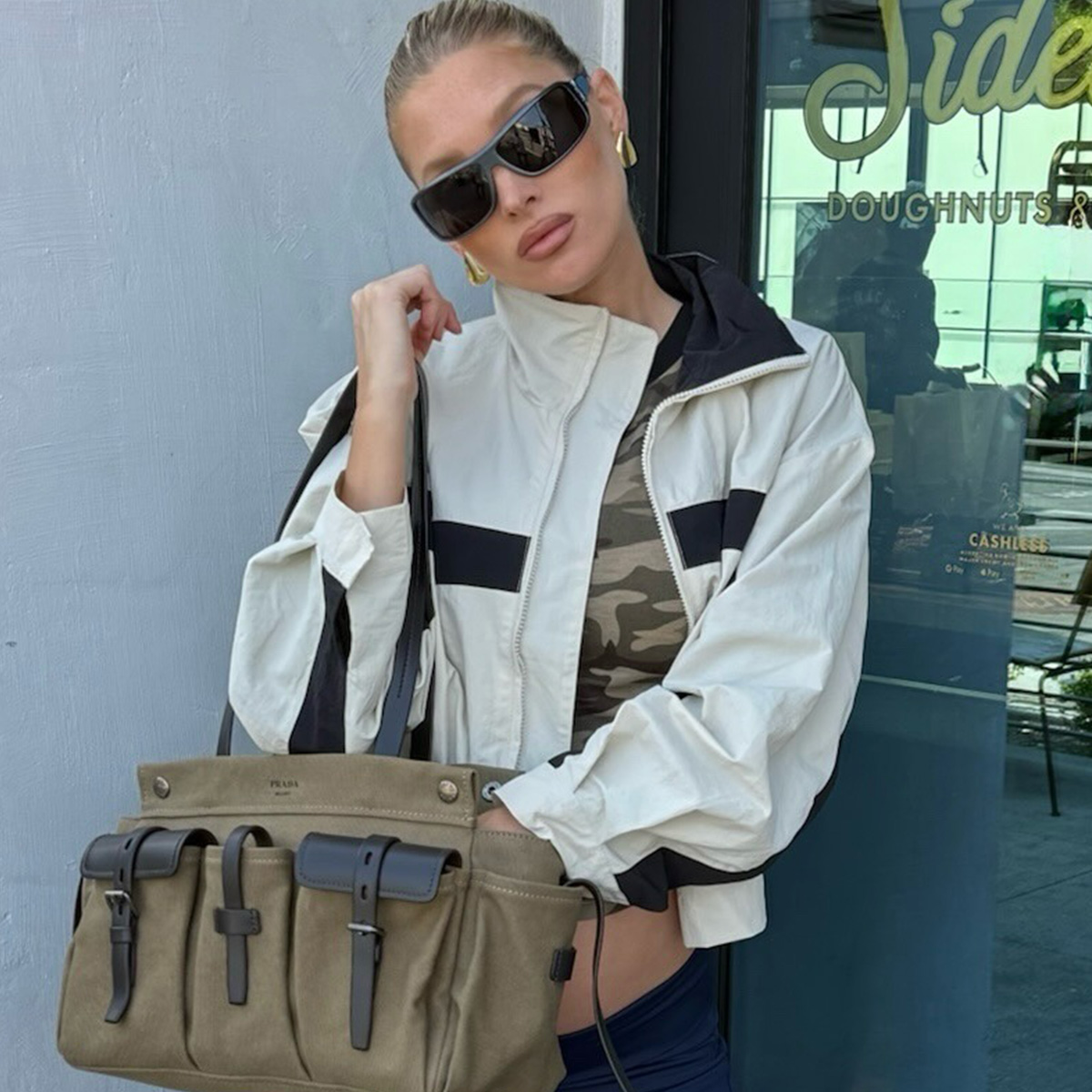 Elsa Hosk wearing a windbreaker, a camo T-shirt, Adidas track pants, Maison Margiela Tabi ballet flats, and a Prada Route bag.