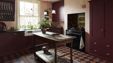 A cosy burgundy kitchen layered with rugs and cafe curtains 