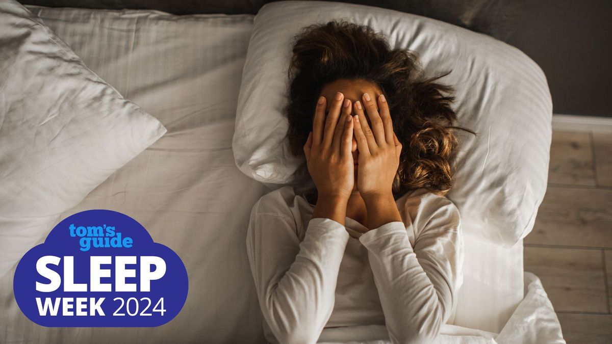 A woman lays back on her bed with her hands placed over her face