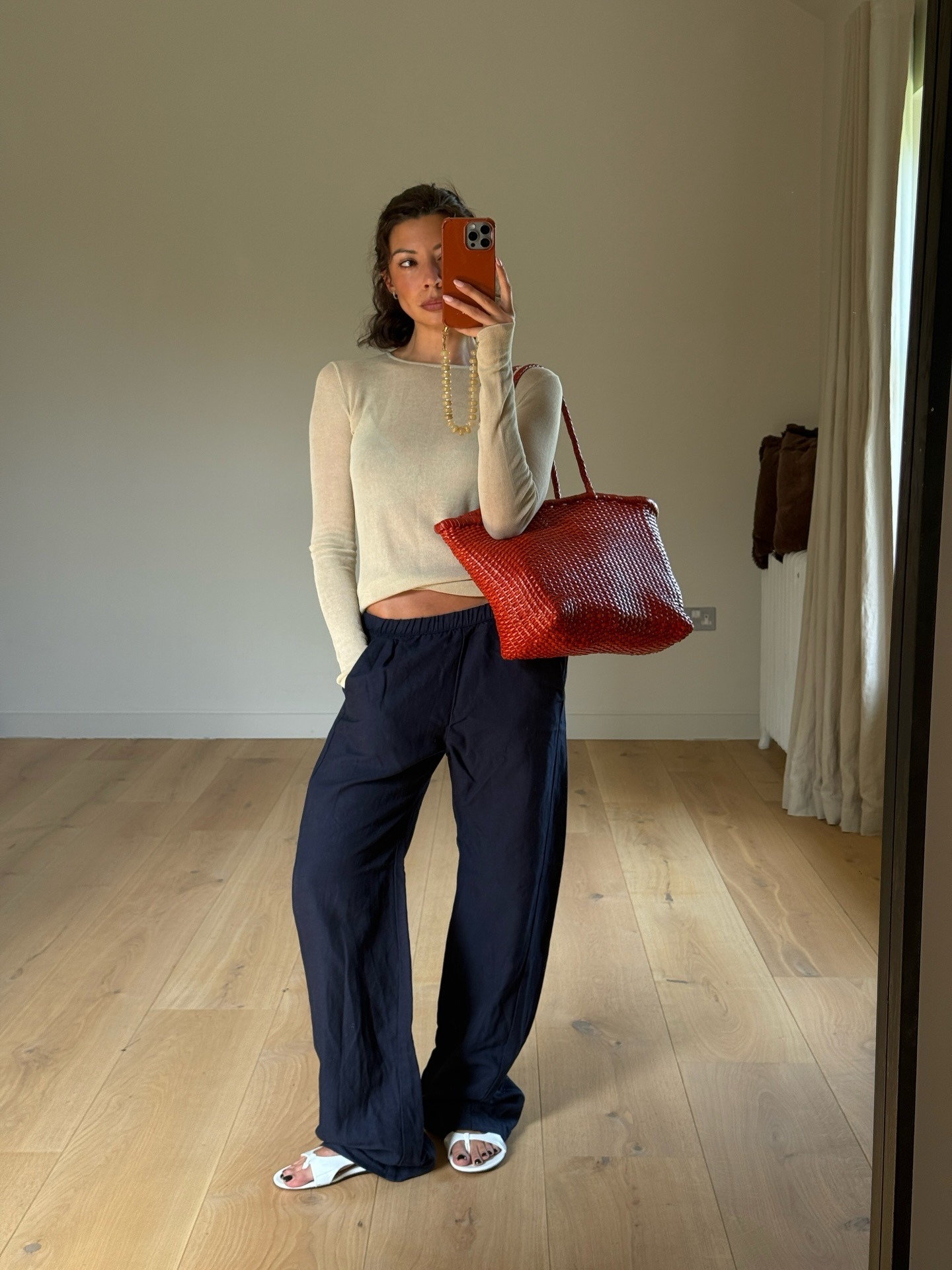 Marianne wearing a navy linen trousers, a top and a red woven bag.
