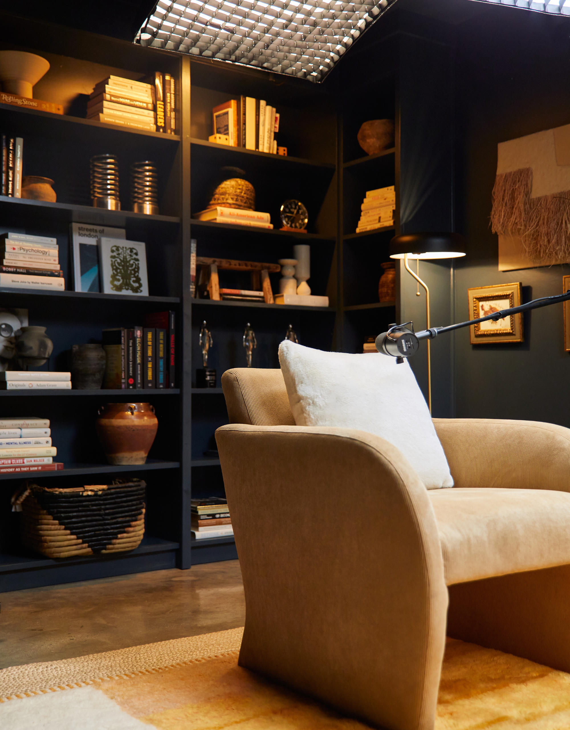 Jay Shetty's podcast studio, with dark walls, antique accessories, a beige arm chair and professional lighting
