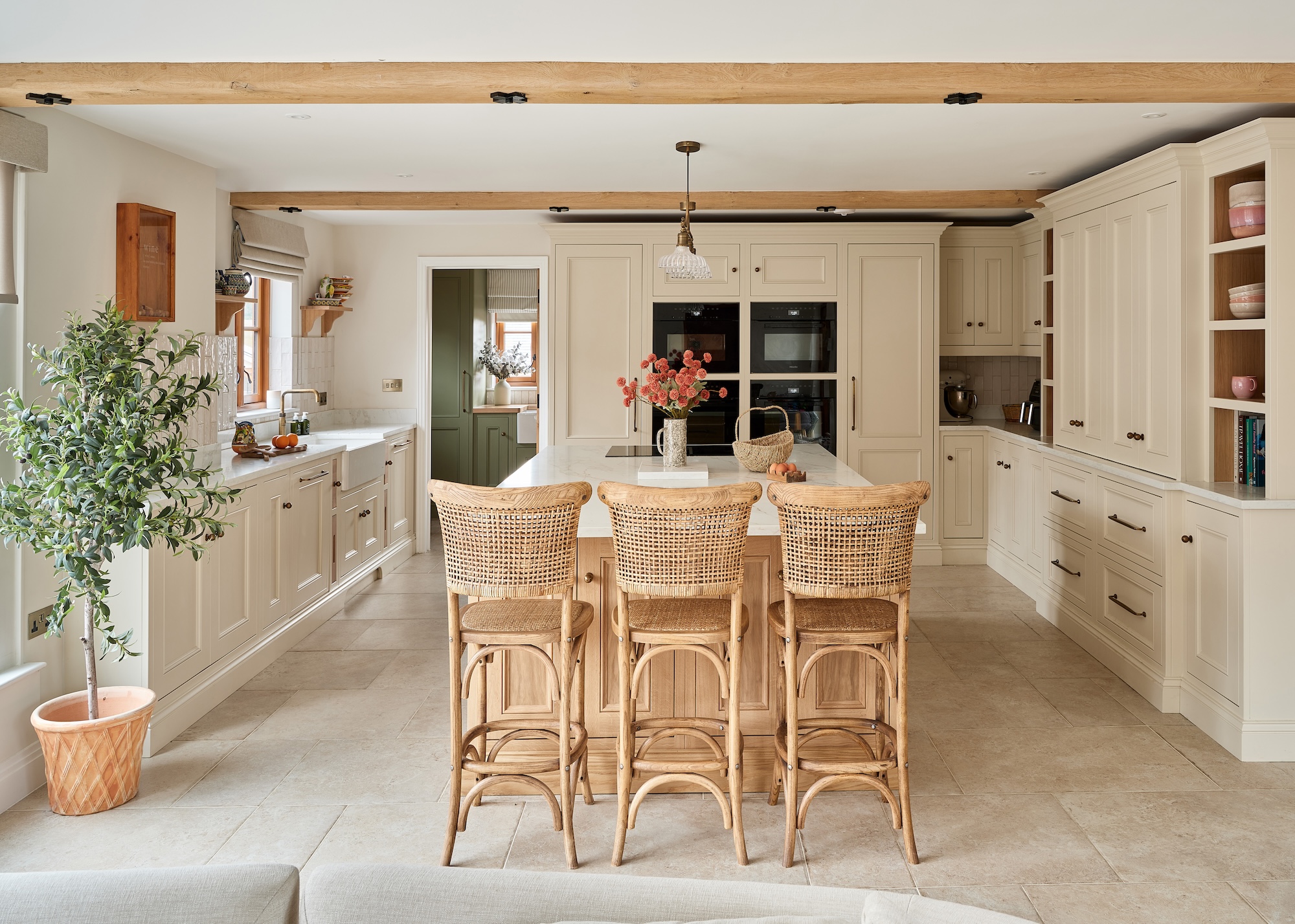 A kitchen with rattan bar stools beside a kitchen island. There is also a large olive tree beside the window