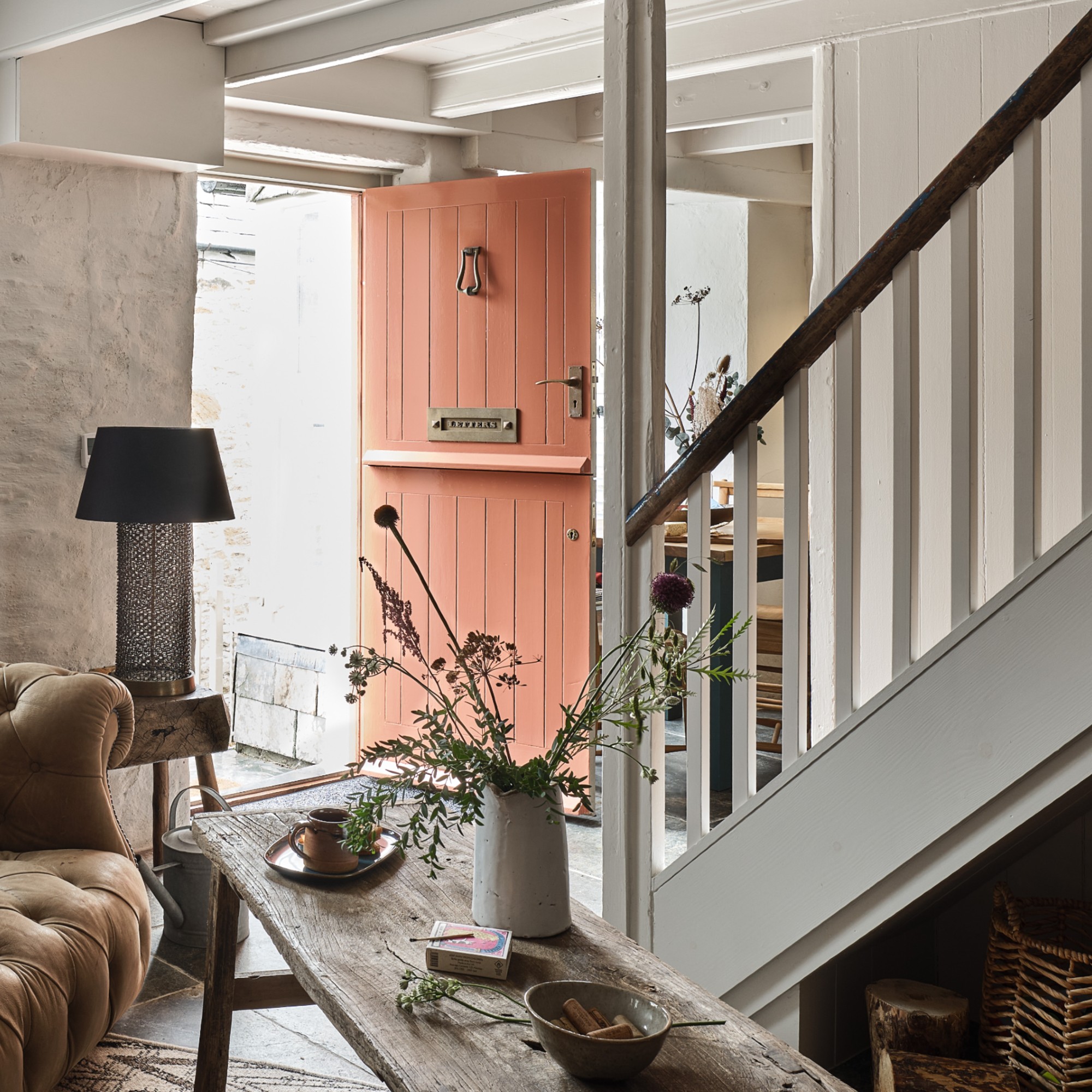 A living room in a cottage with an open front door painted in a terracotta shade