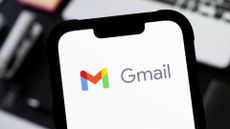 Up-close picture of the Gmail logo and branding pictured on a smartphone, with laptop placed on desk in background.