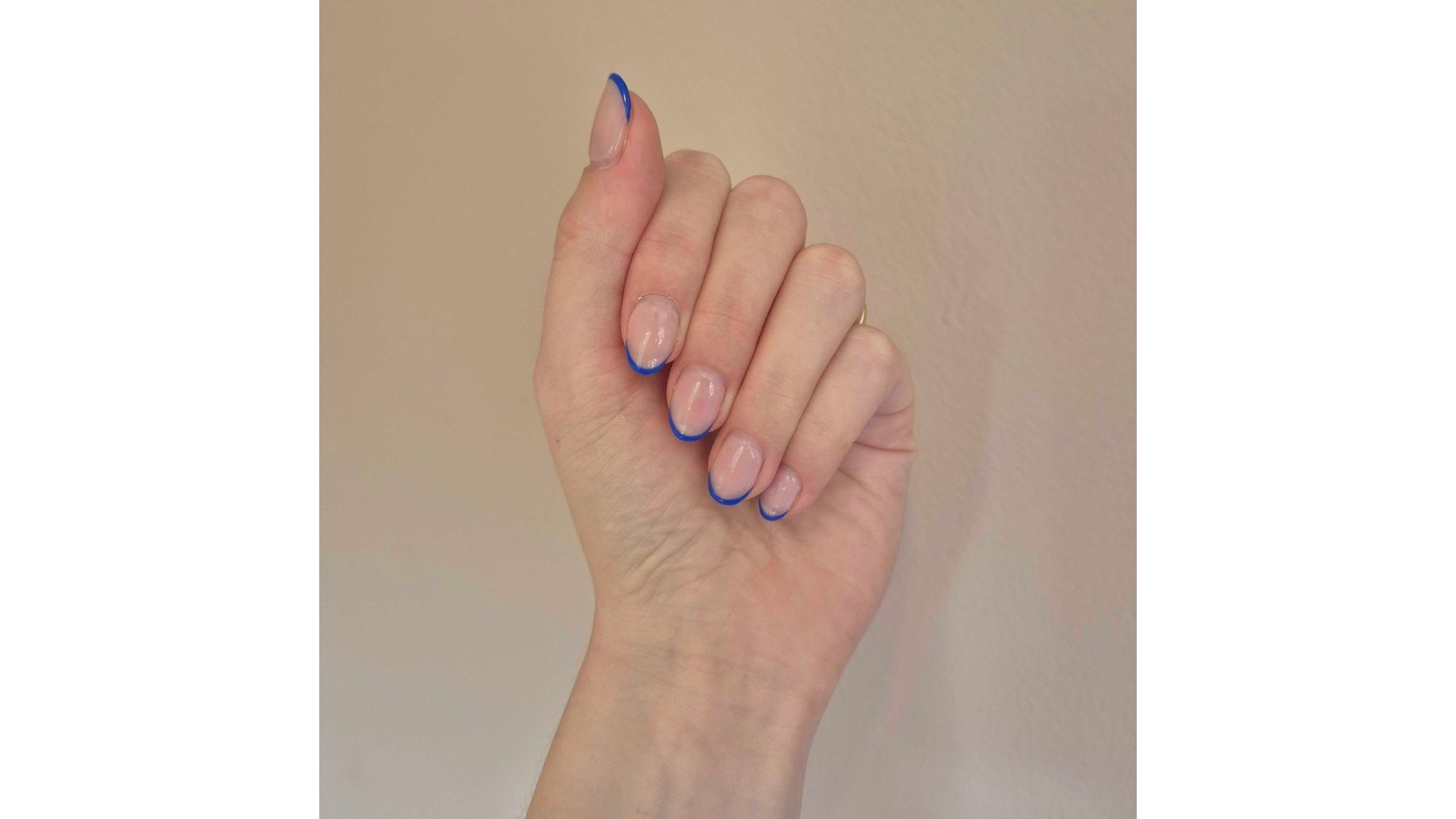 A close-up of Digital Beauty Writer, Naomi Jamieson's hand, which features a bright blue French tip manicure, pictured in front of a cream background