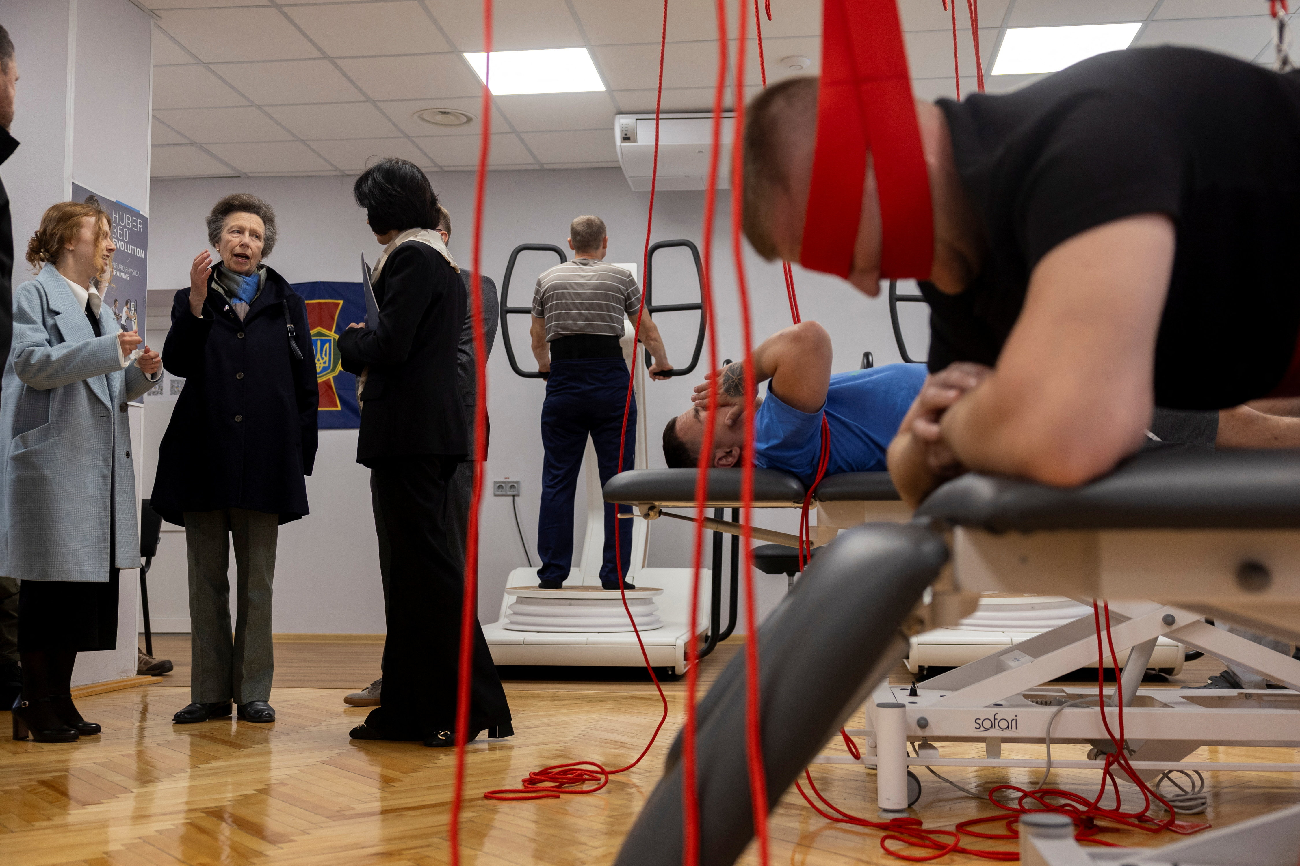 Princess Anne talking to women in a rehabilitation center with men laying on equipment exercising behind them