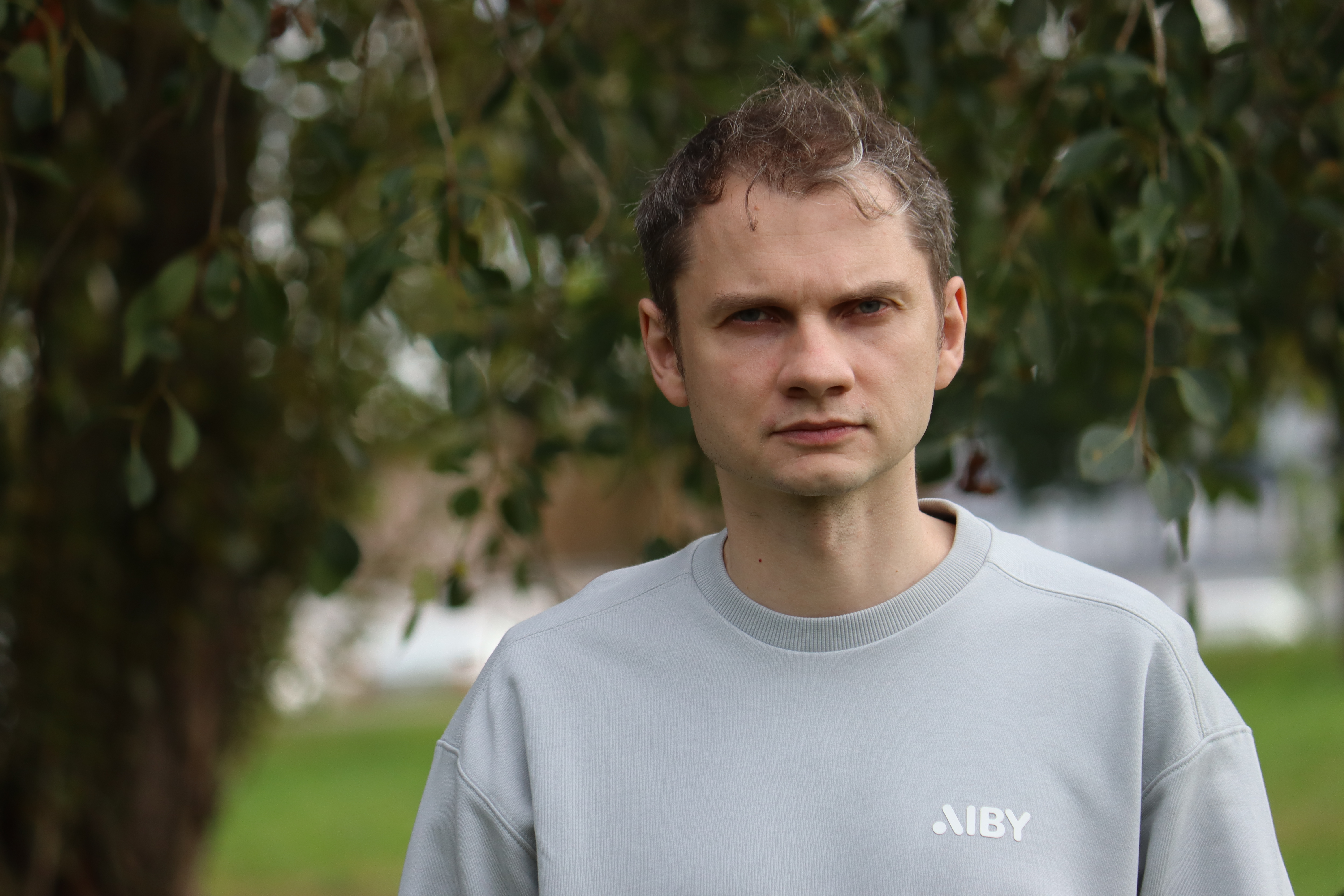 Headshot of a male in a gray sweater in front of a tree