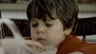 A little boy with a black bowl cut eats cereal.