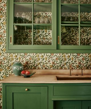 Green glazed kitchen cabinet fitted on a wallpapered wall