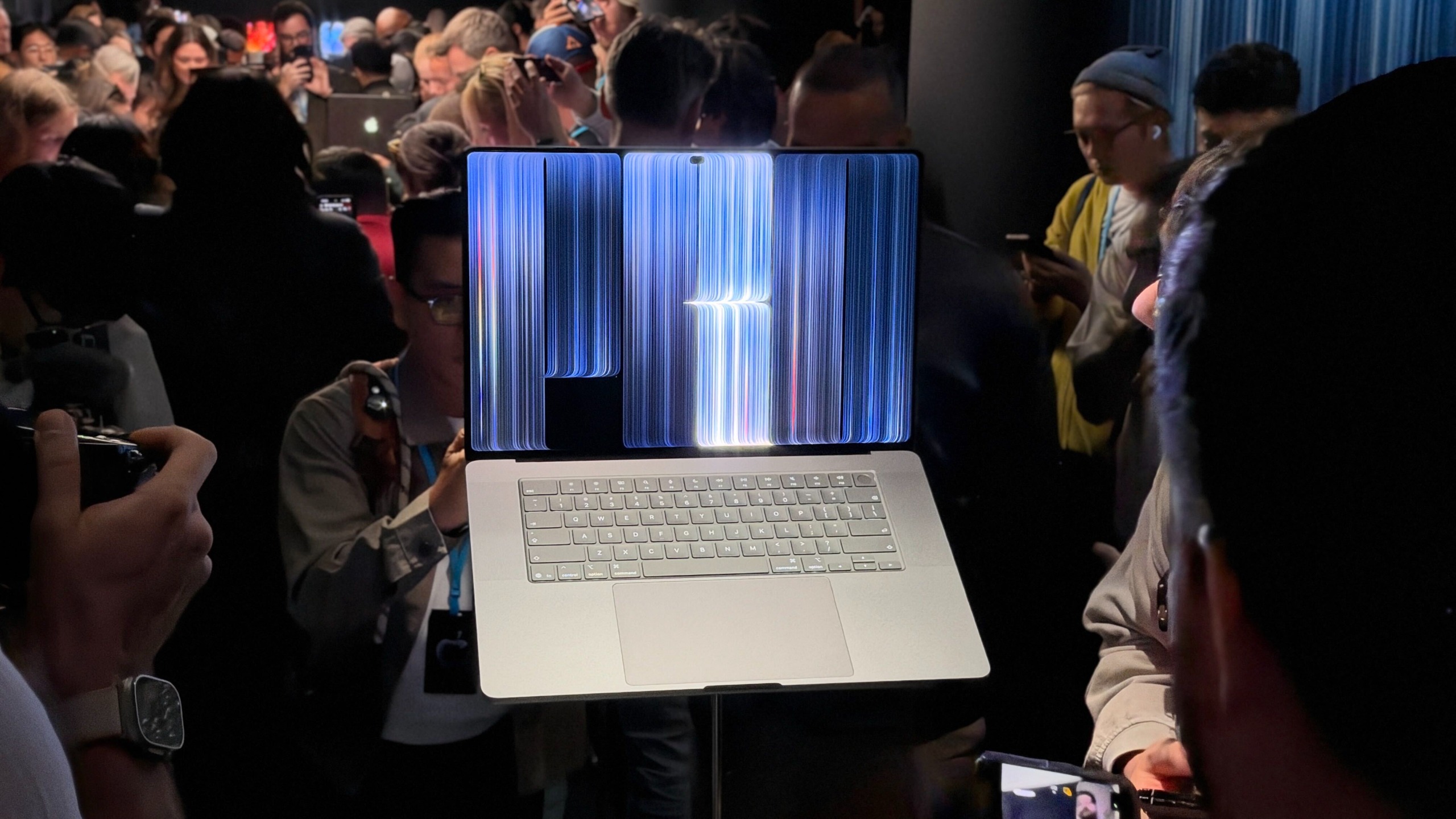 The MacBook Pro PROLED XDR on a stand at its launch event, with people crowding around it