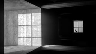 Monochrome image of a silhouette of a person in a window, light casting shadows on the wall