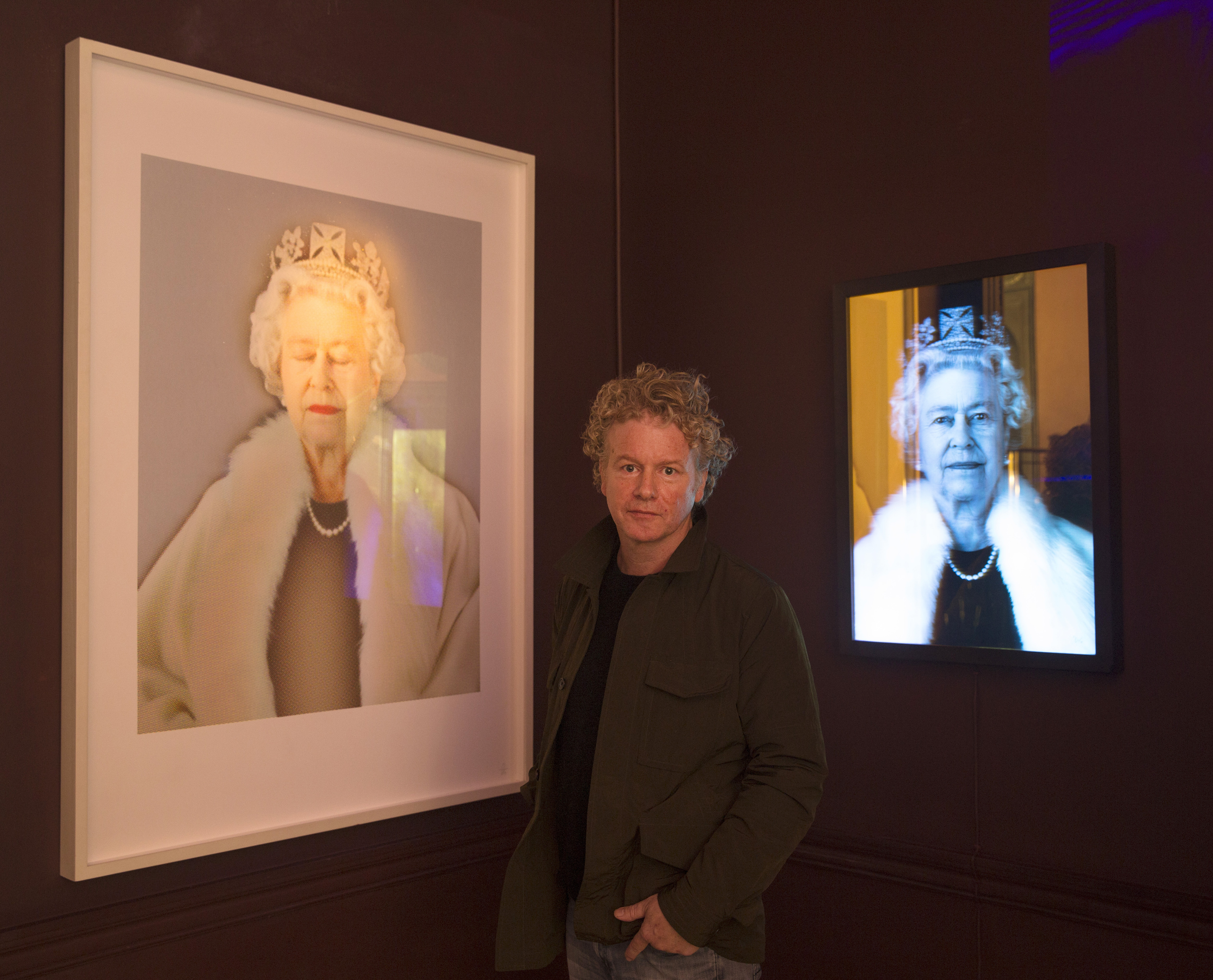 Artist Chris Levine posing with two portraits of the late Queen