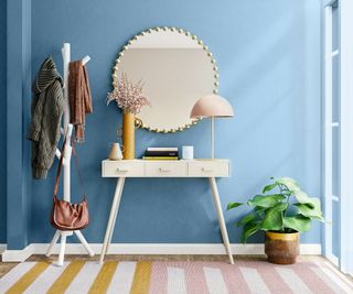 hallway with blue walls and pink and yellow striped rug, white console table, coat stand and round mirror