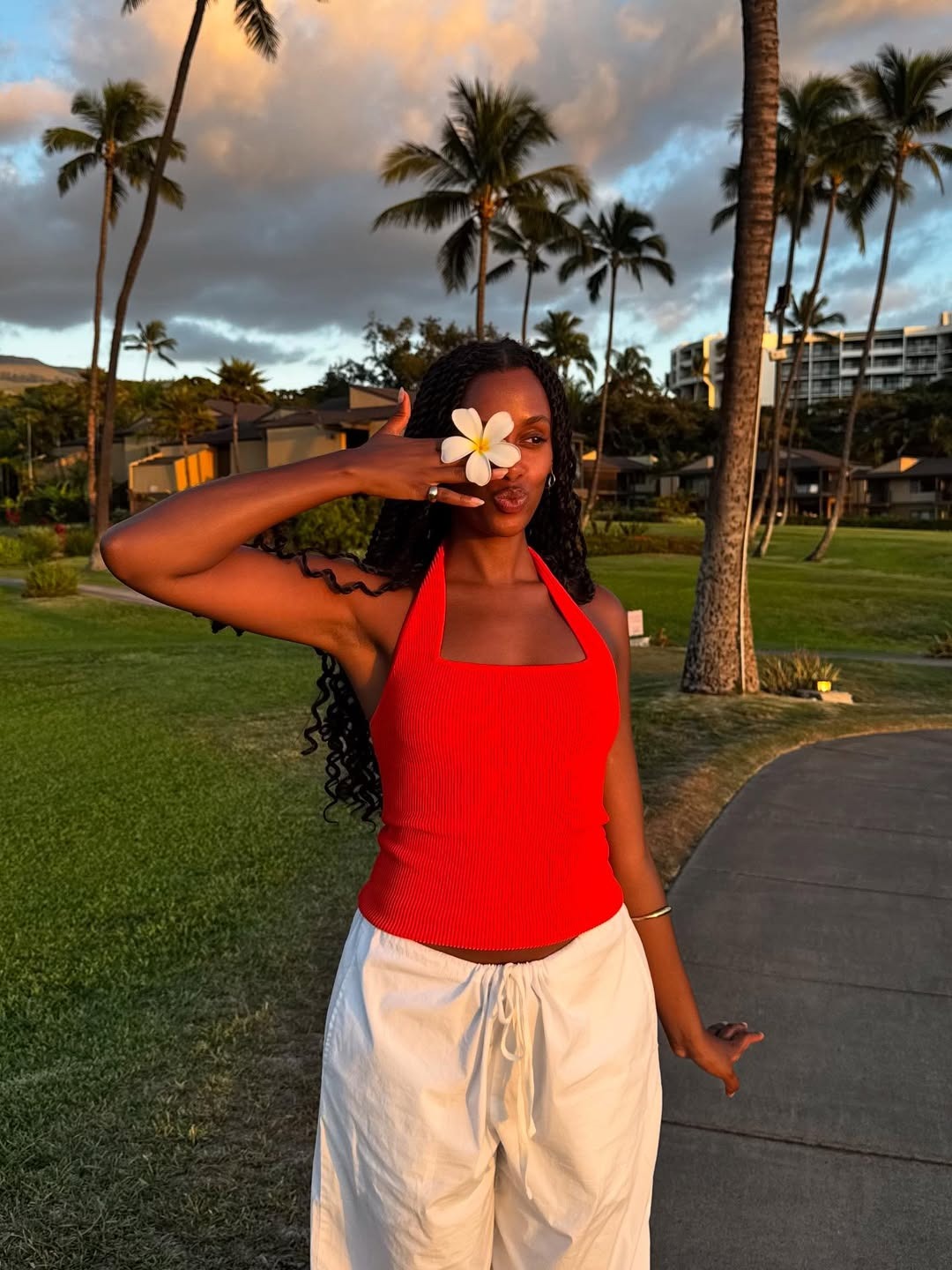 An image of a woman holding a flower in front of her face on an island.