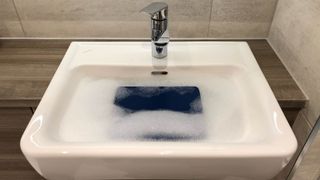 A mousepad submerged under soapy water in a sink