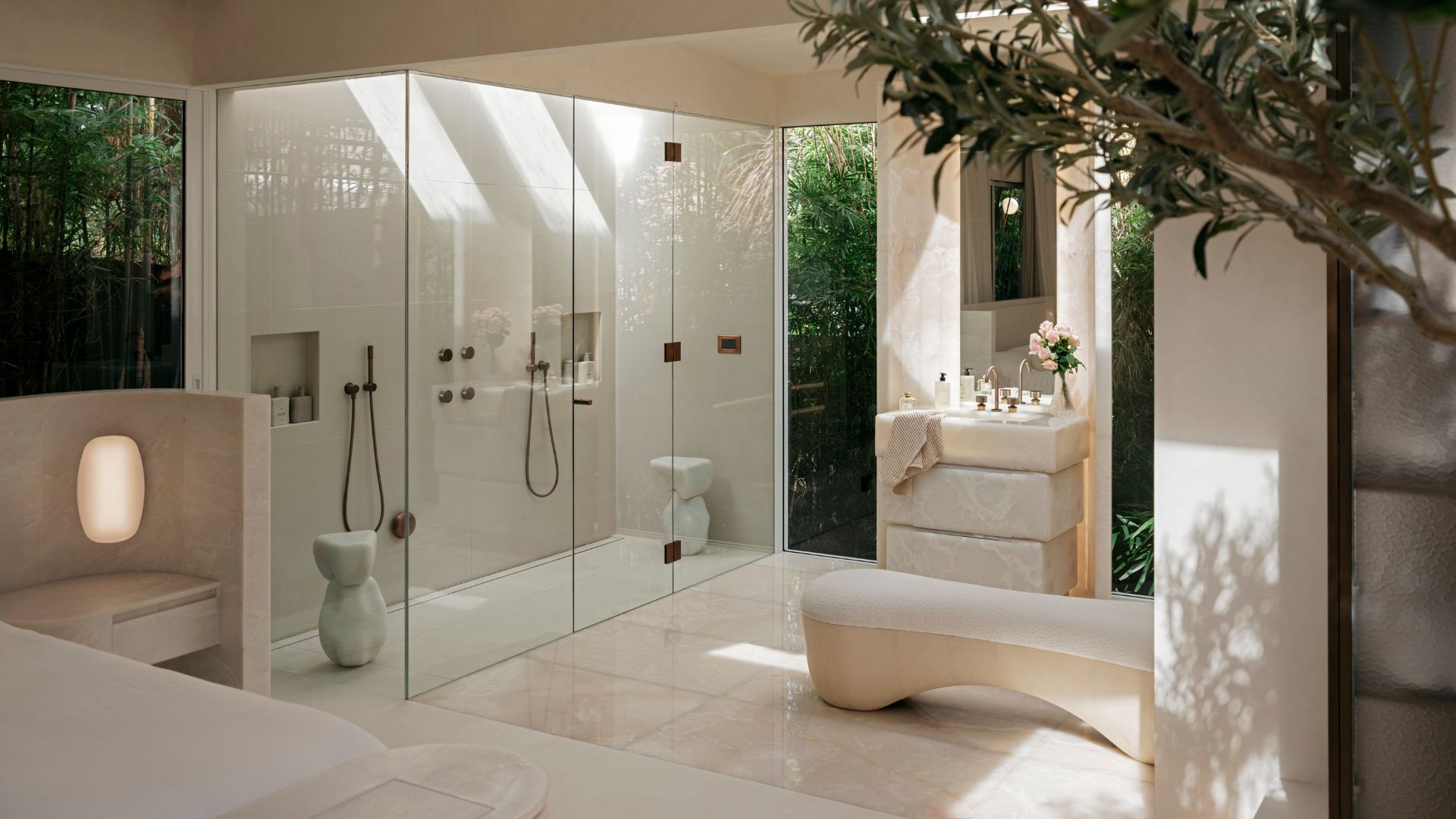 A white bathroom with a shower room, a bench, a stone sink, and a potted tree