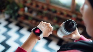 Woman looking down at heart rate metric on fitness tracker and holding water bottle