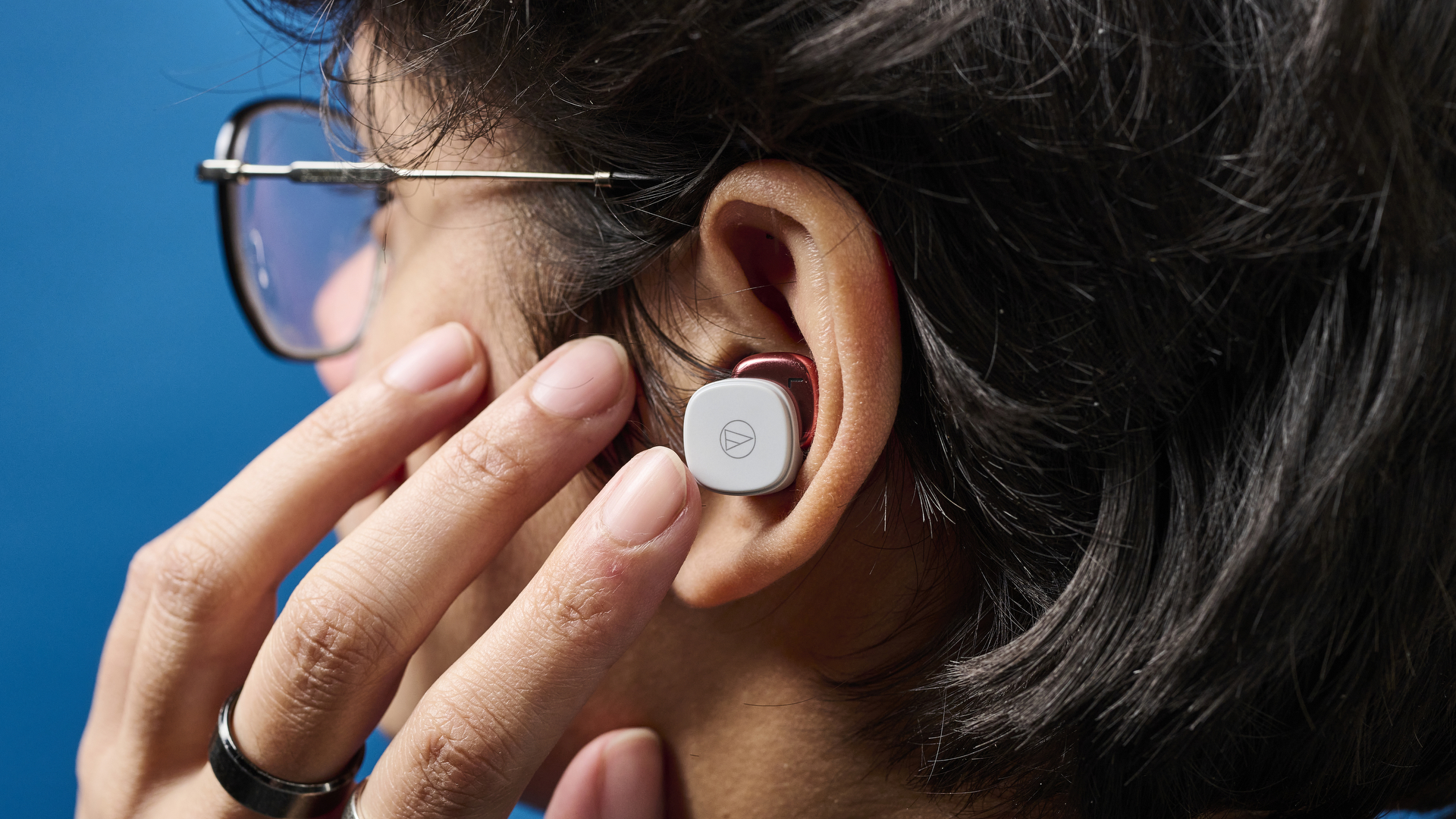 A person tapping an Audio-Technica ATH-SQ1TW earbud in their left ear