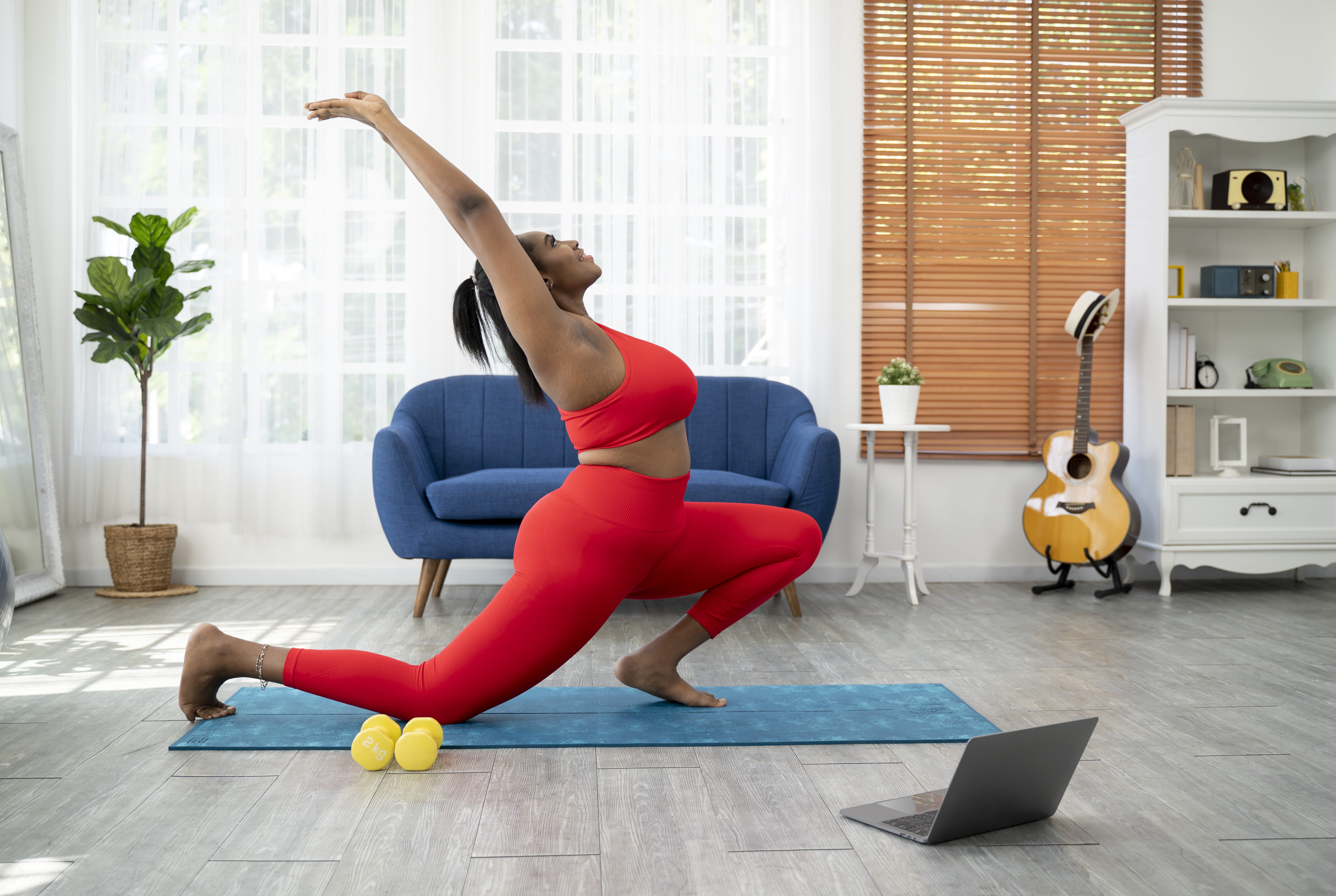 Woman practicing yoga at home with laptop and weights