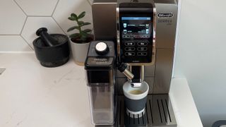 De’Longhi Dinamica Plus on a kitchen countertop with milk in the frofther, ready to pour an espresso