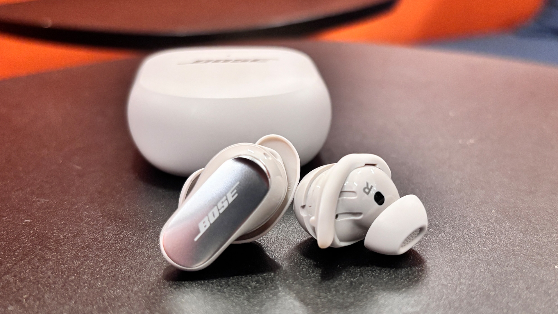 Bose QuietComfort Ultra Earbuds (2nd Gen) wireless earbuds on shiny black table in front of charging case