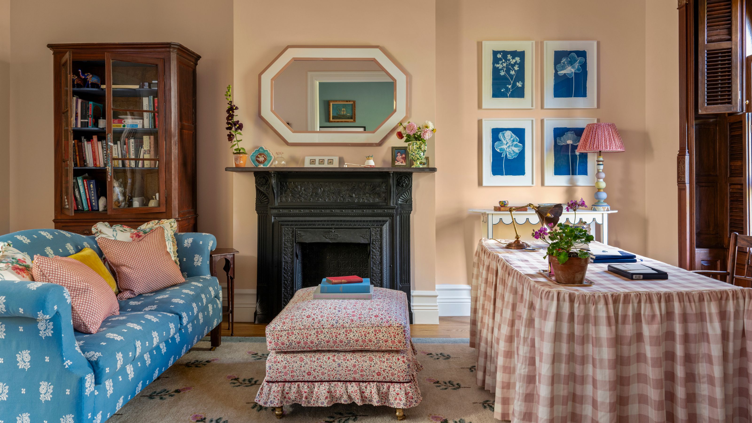 a pale pink home office with an original cast iron fireplace, gingham skirted desk and a blue floral sofa