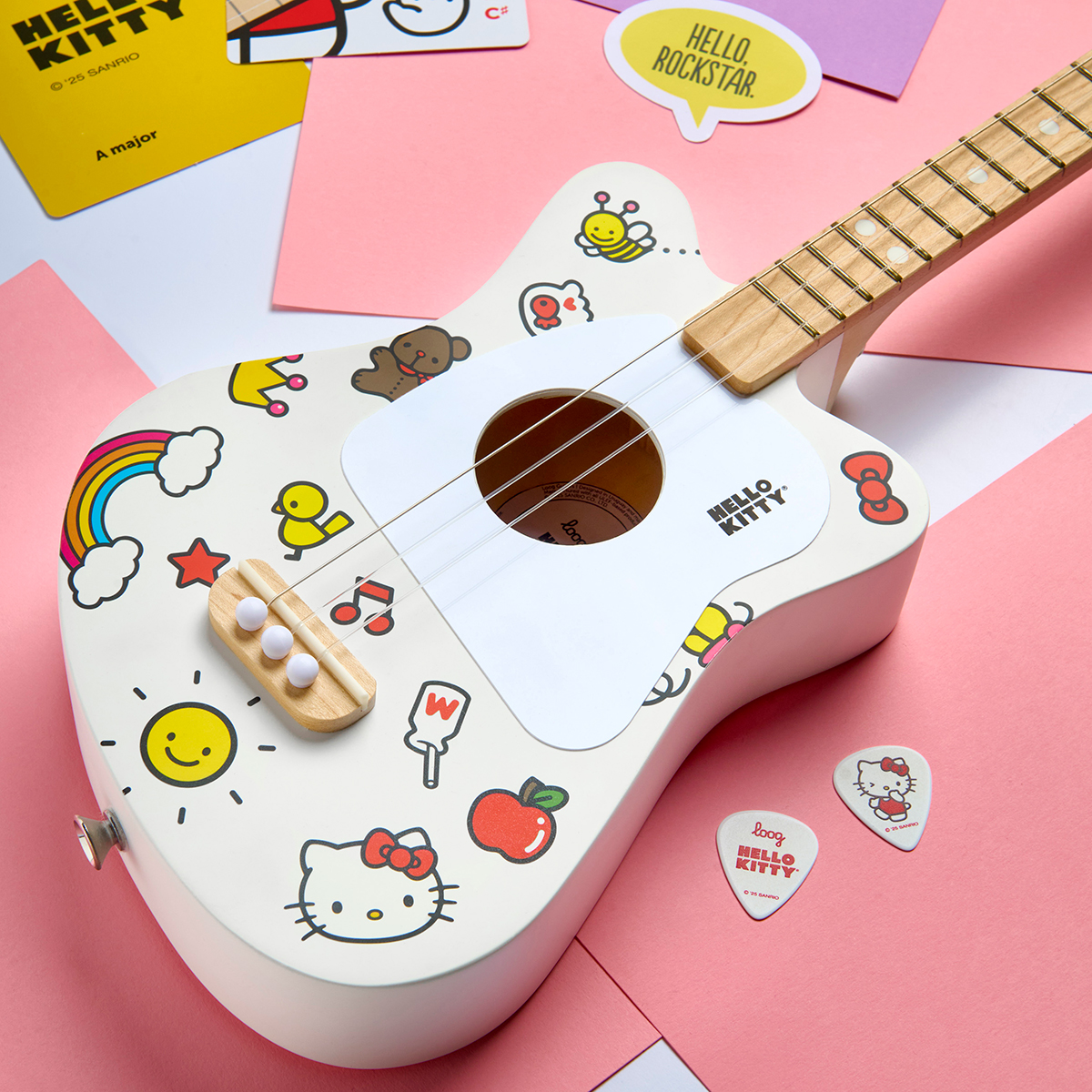 A Loog Hello Kitty Mini Acoustic guitar, sat atop a number of bright pink sheets of paper