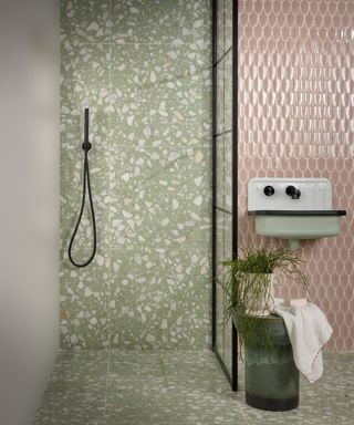 A pink and green bathroom with green terrazzo tiles drenching the shower area and the floor of the whole bathroom and pink wall tiles behind the sink