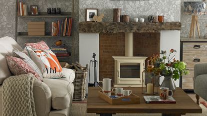 Living room with cream sofa, grey patterned wallpaper, cream woodburner, wooden mantlepiece and coffee table