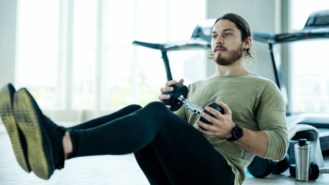 A man performing a weighted abs exercise with a dumbbell