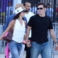 Dua Lipa and Calum Turner exit the World Cup holding hands. Dua wears straight-leg jeans with snakeskin shoes and a white halterneck top.
