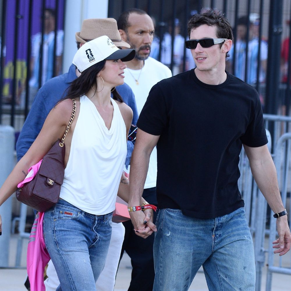 Dua Lipa and Calum Turner exit the World Cup holding hands. Dua wears straight-leg jeans with snakeskin shoes and a white halterneck top.