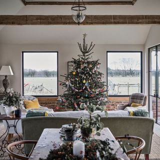 Large decorated Christmas tree between windows framed by seating area in living room