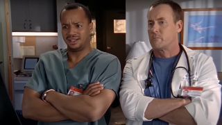 Turk and Dr. Cox standing cross-armed in Sacred Heart break room in Scrubs