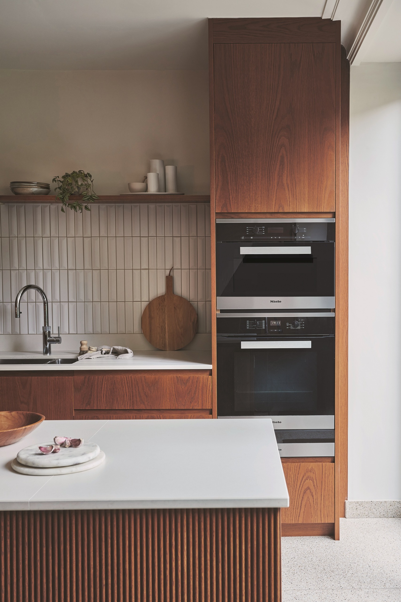 a timber and off white kitchen with a tiled backsplash and fluted island