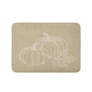 A beige bath mat with a pumpkin illustration