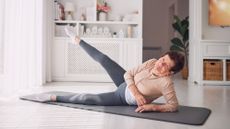 Woman lies on her side on an exercise mat in a domestic setting, with one leg raised