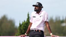 Sahith Theegala leans up against an advertising board by a tee box at the Butterfield Bermuda Championship in 2025