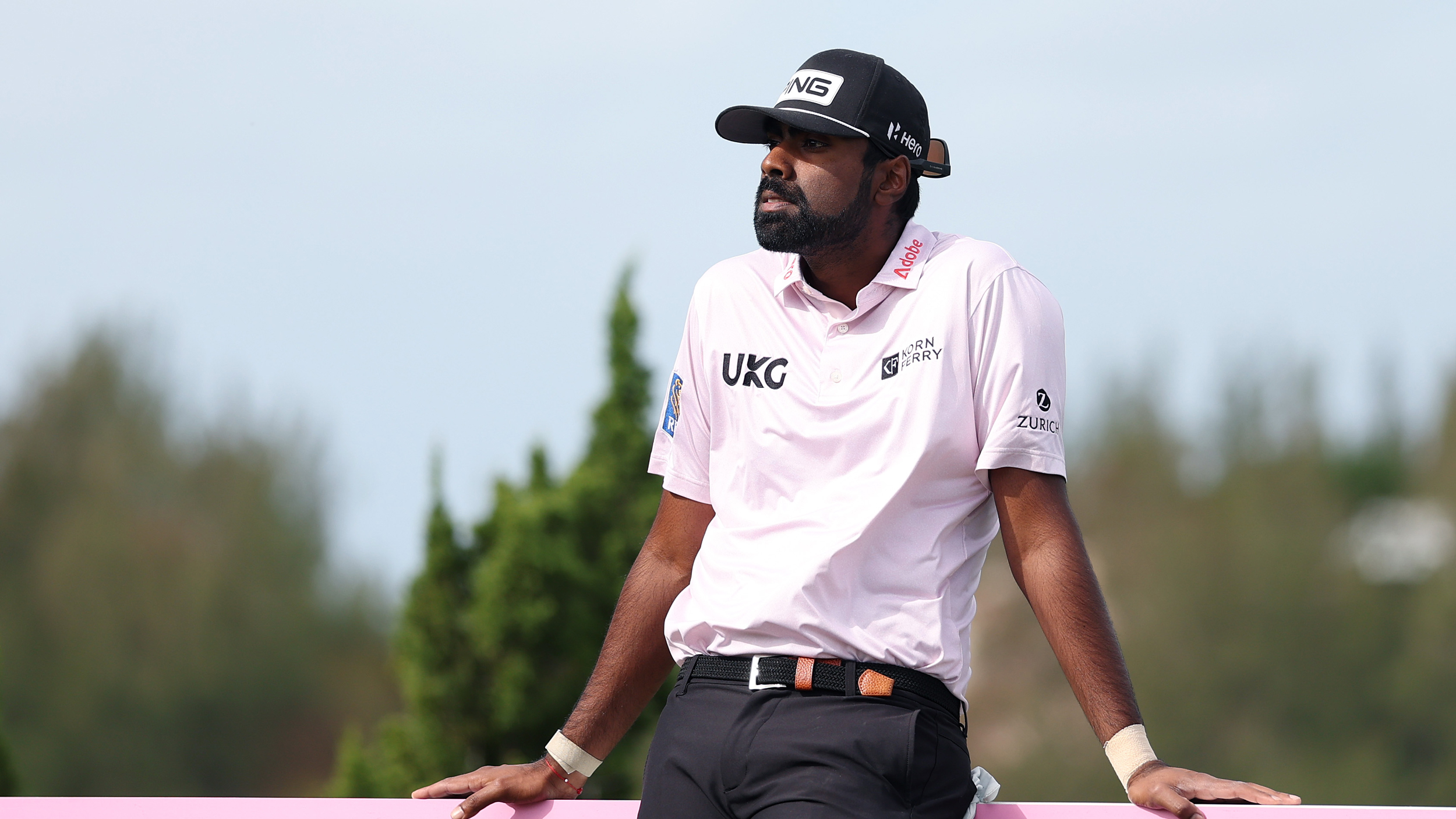 Sahith Theegala leans up against an advertising board by a tee box at the Butterfield Bermuda Championship in 2025