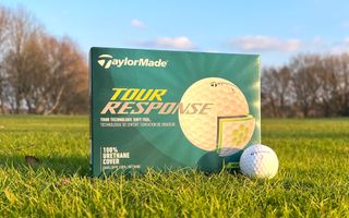 TaylorMade Tour Response 2022 Golf Ball resting on the fairway in its green packaging