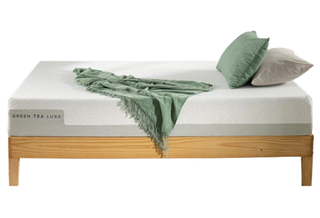 The Zinus Green Tea Luxe Mattress shown on a light wooden bed frame and dressed with green pillows and throws