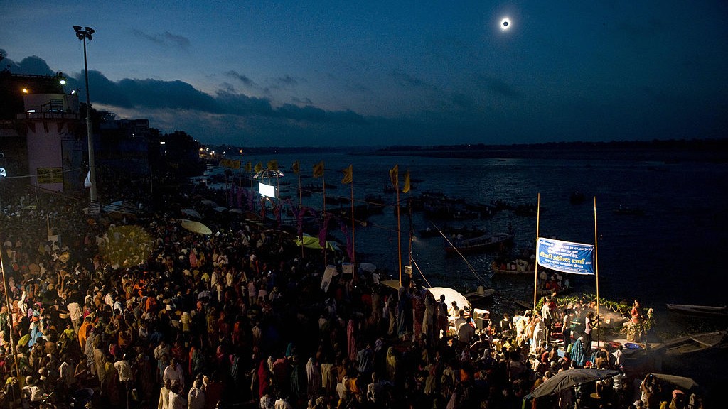 Thousands of people are gathered to watch a solar eclipse in the dark sky above.