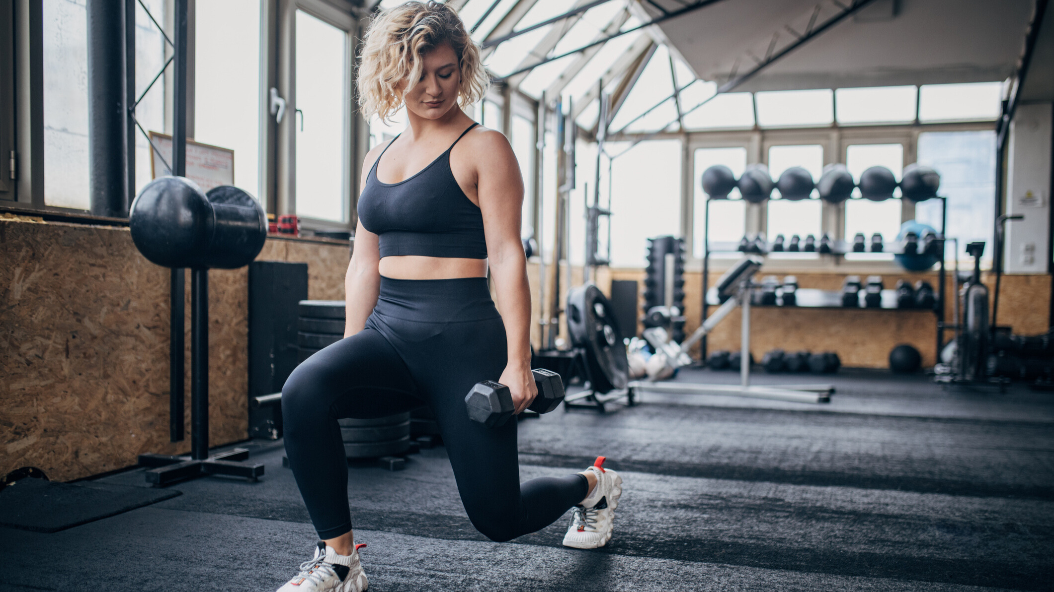 Woman performing lunges while holding dumbbells in a gym